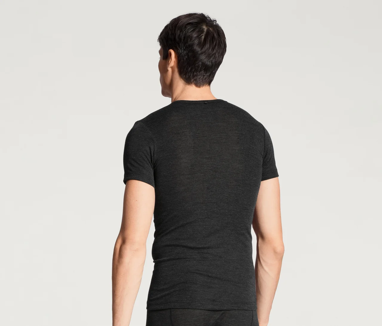 Mann von hinten, der ein dunkelgraues Kurzarm-T-Shirt und eine passende Unterhose trägt und nach rechts blickt.
