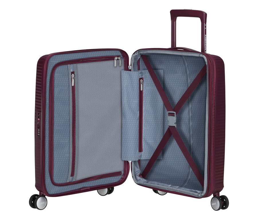 Offener American Tourister Soundbox Spinner Hartschalenkoffer in Wildkirschrot, der die Innenausstattung mit Reißverschlussfächern und Packgurten zeigt.