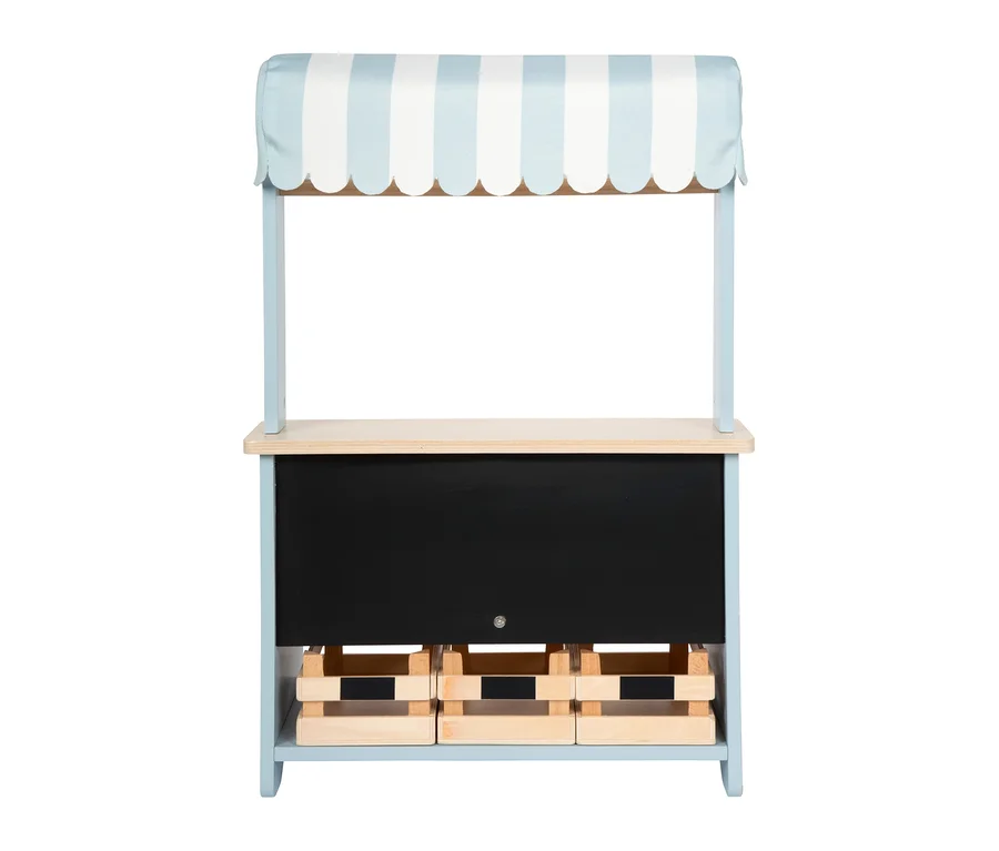 Ein small foot kompakter Kaufladen mit hellblau-weiß gestreiftem Vordach, Holztresen, schwarzer Kreidetafel und drei Holzkisten.