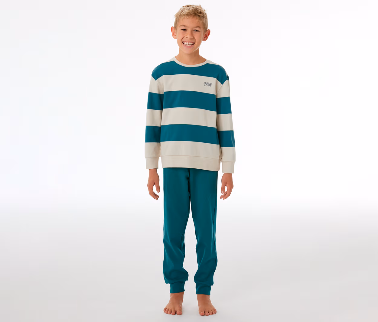 Lächelnder Junge steht in einem gestreiften SCHIESSER Kinder-Interlock-Pyjama in Türkis und Beige.