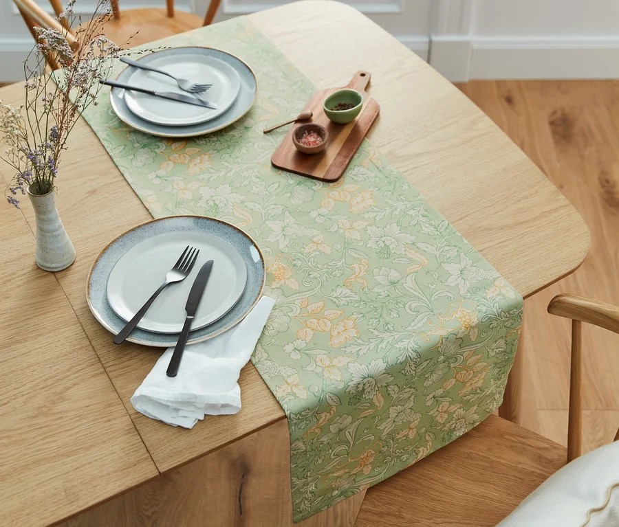 Auf einem Holztisch liegt ein Tischläufer mit grünem Blumenmuster.