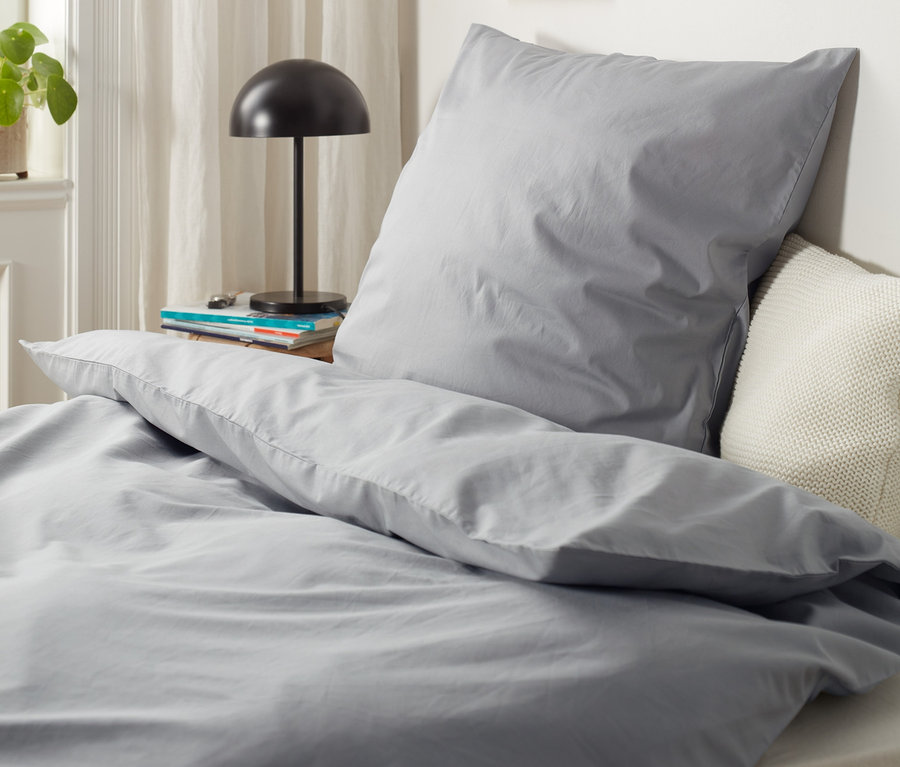 Graue Perkal-Bettwäsche in Normal- und Übergröße auf einem Bett.
