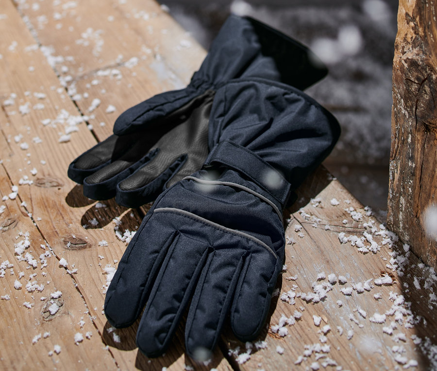 Dunkelblaue Winterhandschuhe liegen auf einer mit Schnee bedeckten Holzfläche.