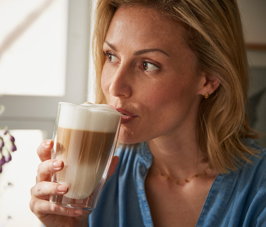 Frau trinkt Latte Macchiato aus einem doppelwandigen Glas.