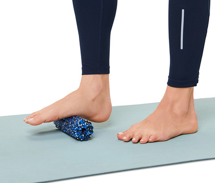 Fuß auf Mini-Faszienrolle auf einer Gymnastikmatte.