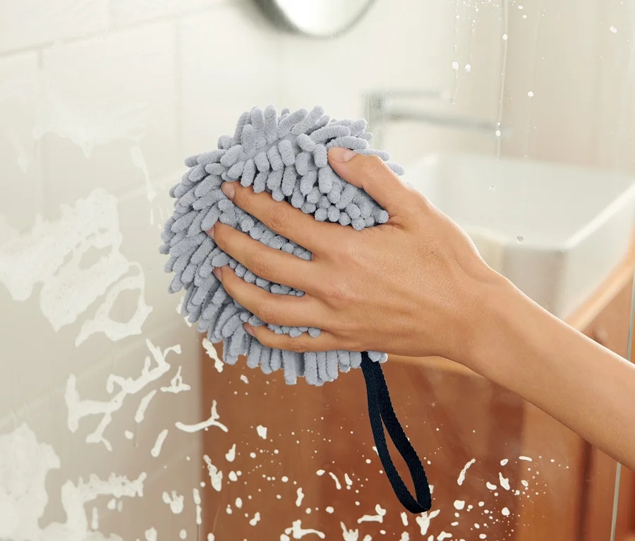 Hand wischt mit Trockenball eine gläserne Duschwand ab.