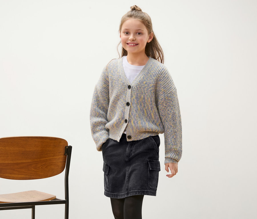 Lächelndes Mädchen posiert in grauem Cardigan und schwarzem Jeansrock.