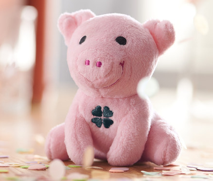 Ein sitzendes, rosa Glücksschwein mit Sound und einem Kleeblatt auf dem Bauch, umgeben von Konfetti.