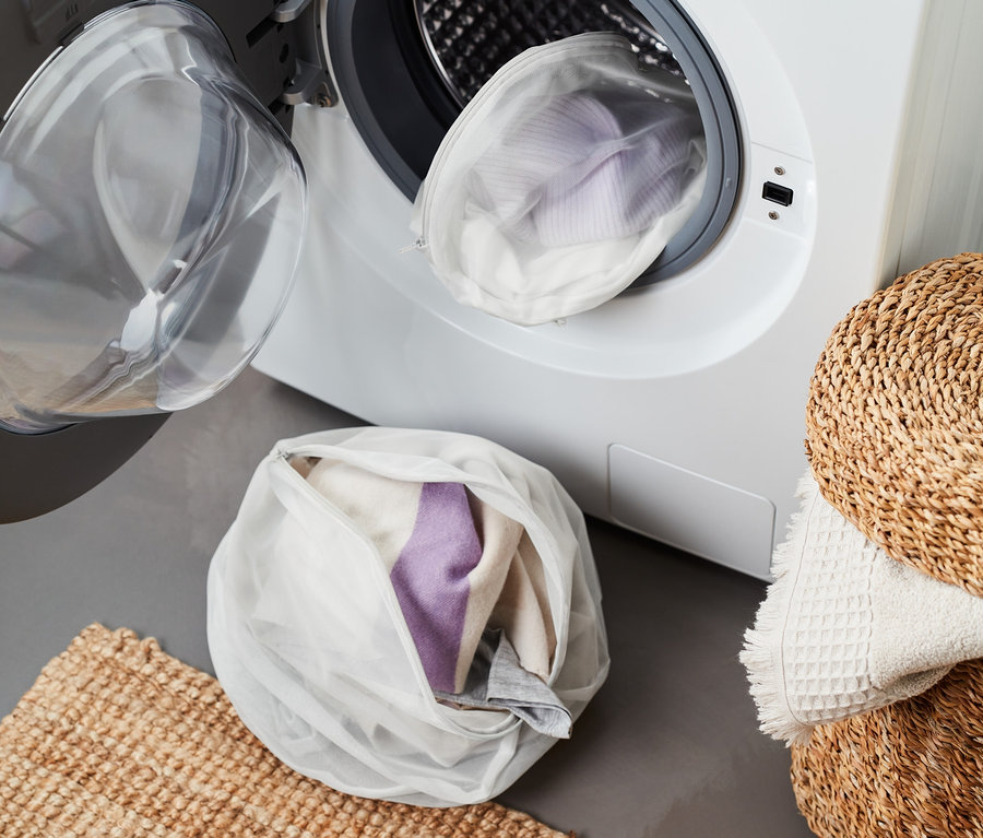 Zwei Wäschenetze, eines in XL, gefüllt mit Kleidung, liegen vor einer offenen Waschmaschine.