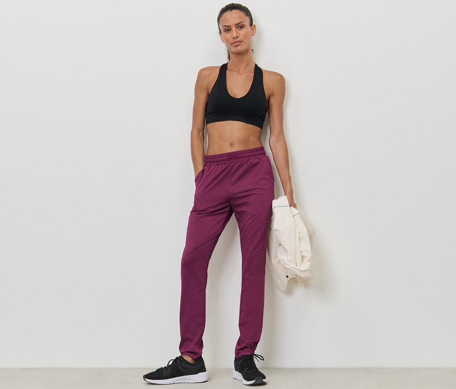 Frau posiert in Sport-BH und beerefarbener Trainingshose.