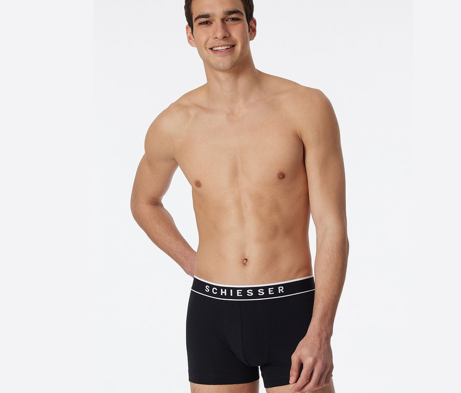 Mann posiert in schwarzen 3 SCHIESSER Shorts mit Bio-Baumwolle.