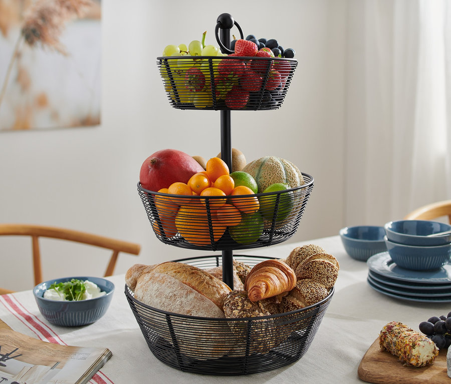 Eine dreistöckige schwarze Etagere aus Metall steht auf einem Tisch, gefüllt mit Obst und Backwaren.