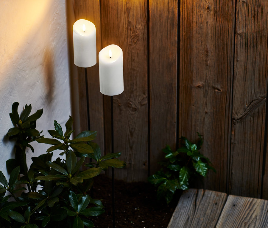 Zwei LED-Echtwachs-Fackeln beleuchten eine Holzwand und Pflanzen.