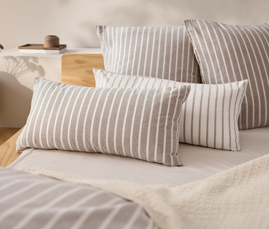 Vier gestreifte Kissen auf einem Bett mit einer beige Tagesdecke.