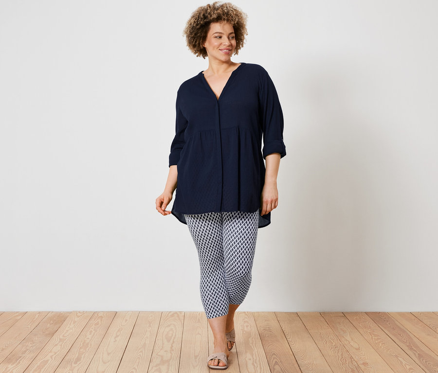 Eine Frau trägt eine Longbluse und bedruckte 3/4-Leggings.