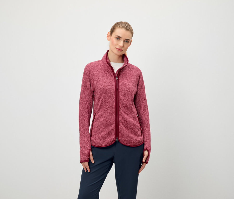 Eine Frau trägt eine langärmlige Fleecejacke mit Reißverschluss und eine dunkelblaue Hose.