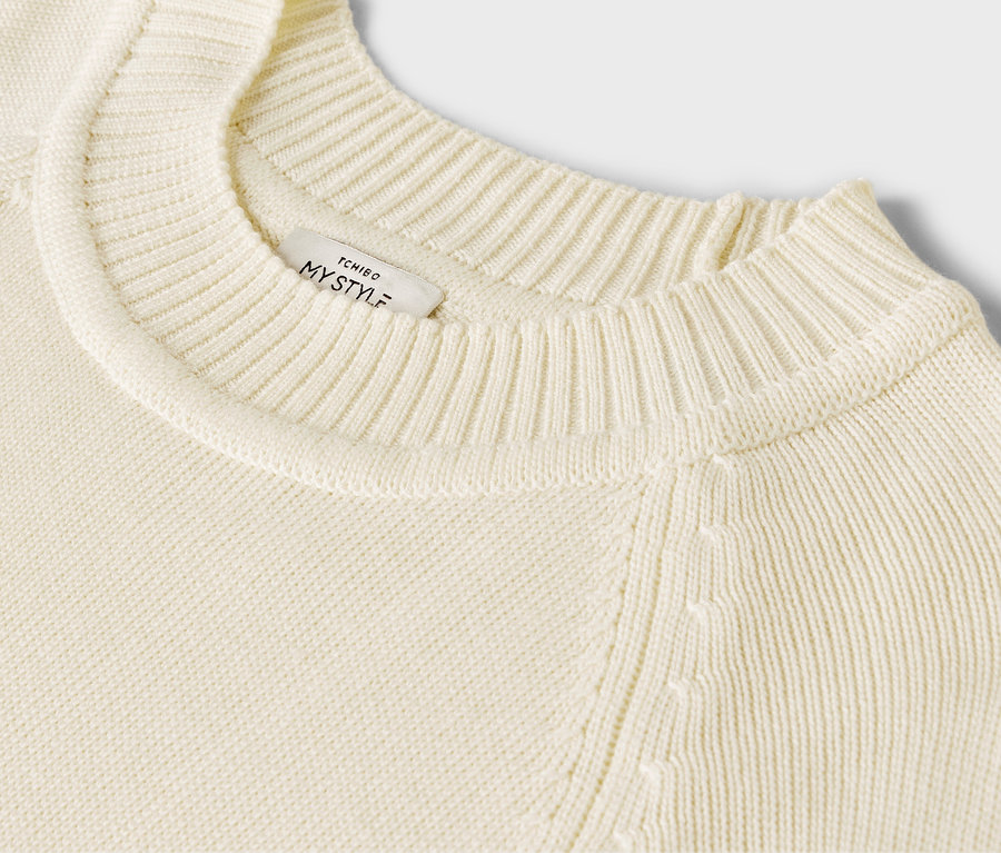 Detailansicht eines cremefarbenen, langen Strickpullovers.