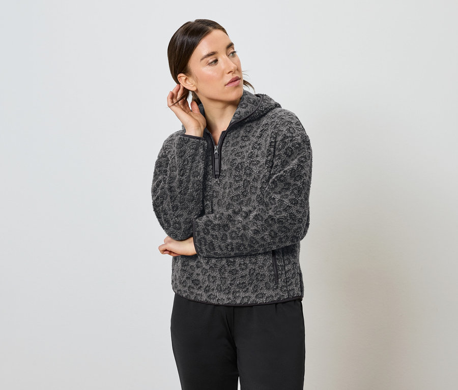 Frau posiert in grau-schwarzem Leopard-Fleece-Hoodie und schwarzer Hose.