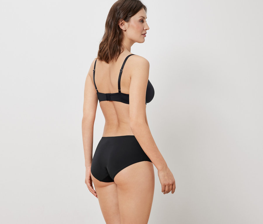 Frau mit dem Rücken zur Kamera trägt einen schwarzen BH und Unterhose.