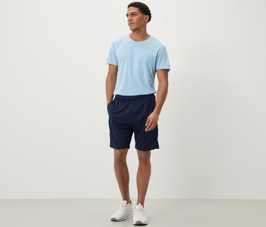 Ein Mann steht und trägt Sportshorts und ein T-Shirt.