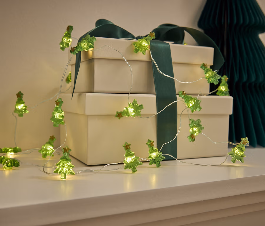 Grüne weihnachtsbaumförmige Lichterkette auf einer weißen Kommode mit Geschenken und einem Papierbaum.