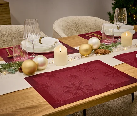 Ein gedeckter Tisch mit roten Tischsets, einem weißen Tischläufer, Kerzen, Gläsern und Weihnachtskugeln.