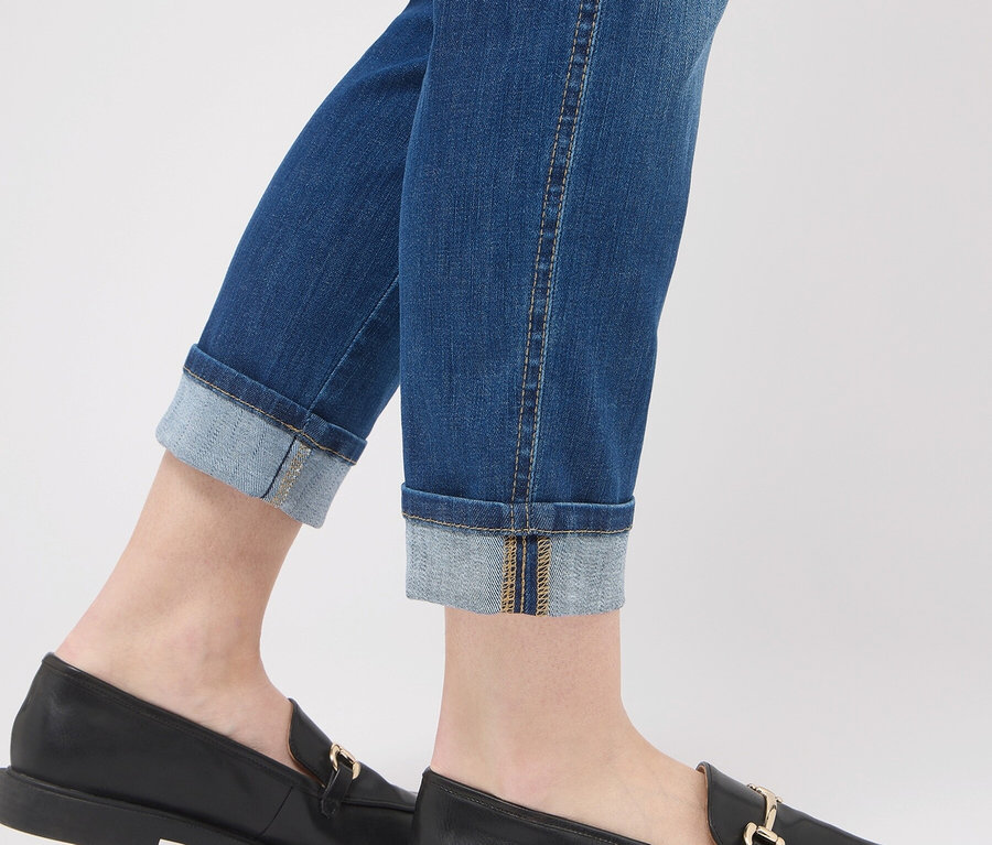 Beine in blauen Jeans mit hochgekrempelten Hosenbeinen und schwarzen Lederloafers mit goldener Schnalle.