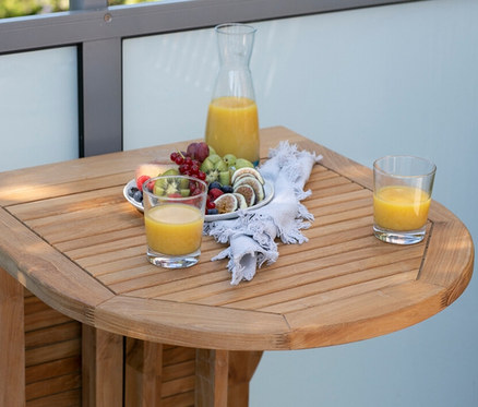 Auf einem deVries Balkontisch, Teak, 60 x 120 stehen Gläser mit Saft und ein Teller mit Früchten.