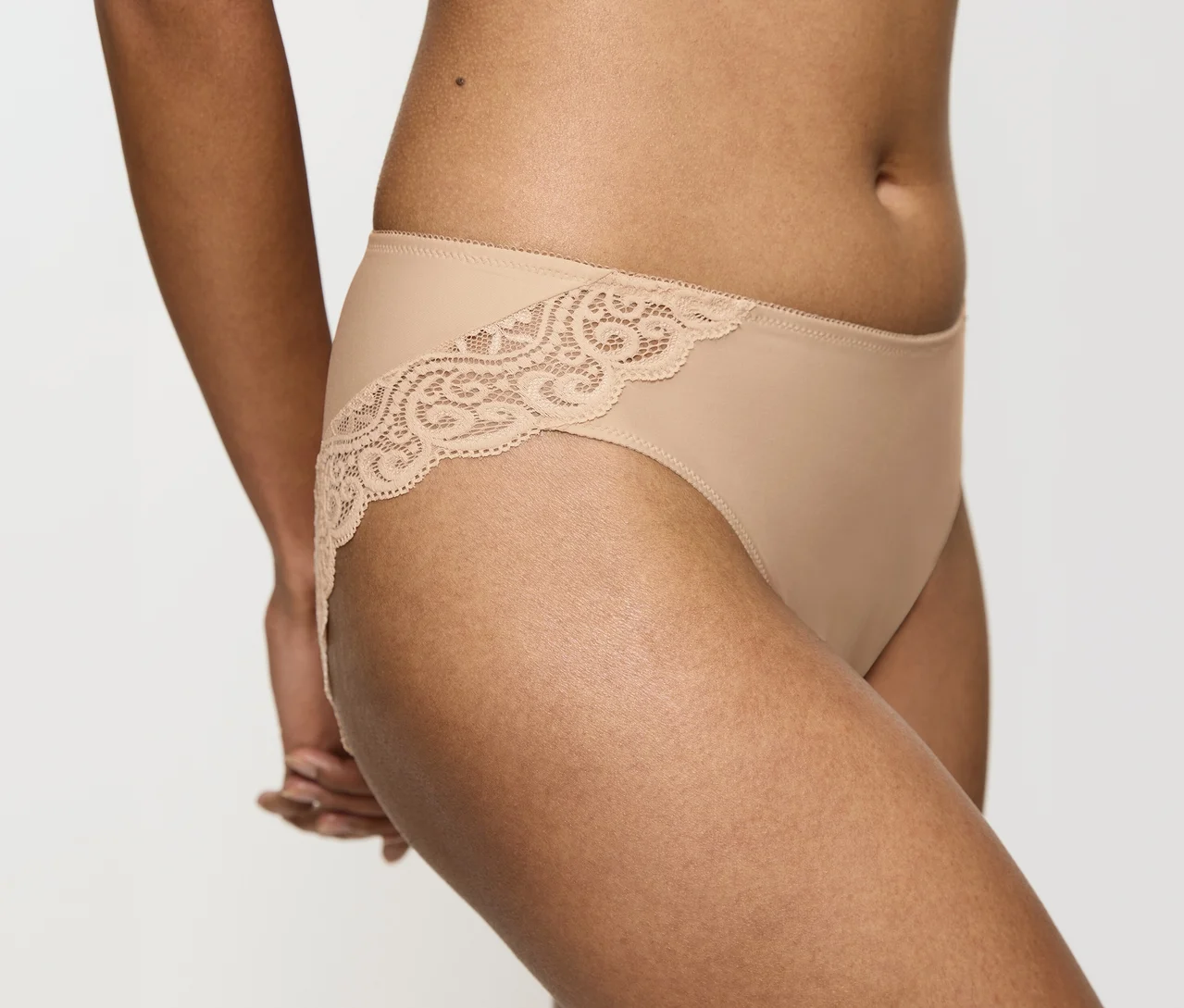 Eine Person trägt einen hautfarbenen Triumph Amourette Tai Slip mit Spitzenbesatz an den Seiten.
