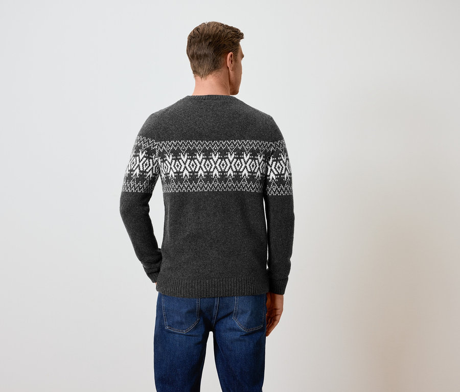 Mann von hinten trägt einen grauen Pullover mit Muster und blaue Jeans.