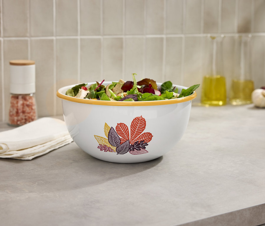 Salatschüssel auf einer Küchentheke neben einer Salzmühle und Ölflaschen.