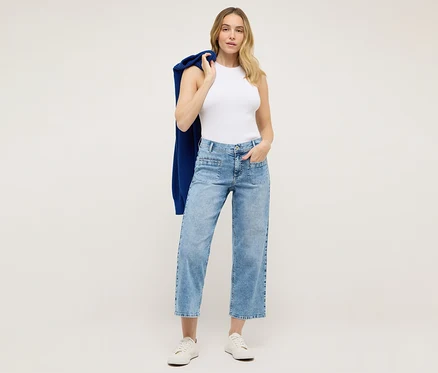 Frau mit hellblauer Angels Denim »Linn Smart« Culotte, weißem Top und blauer Strickjacke über der Schulter, posiert vor hellem Hintergrund.