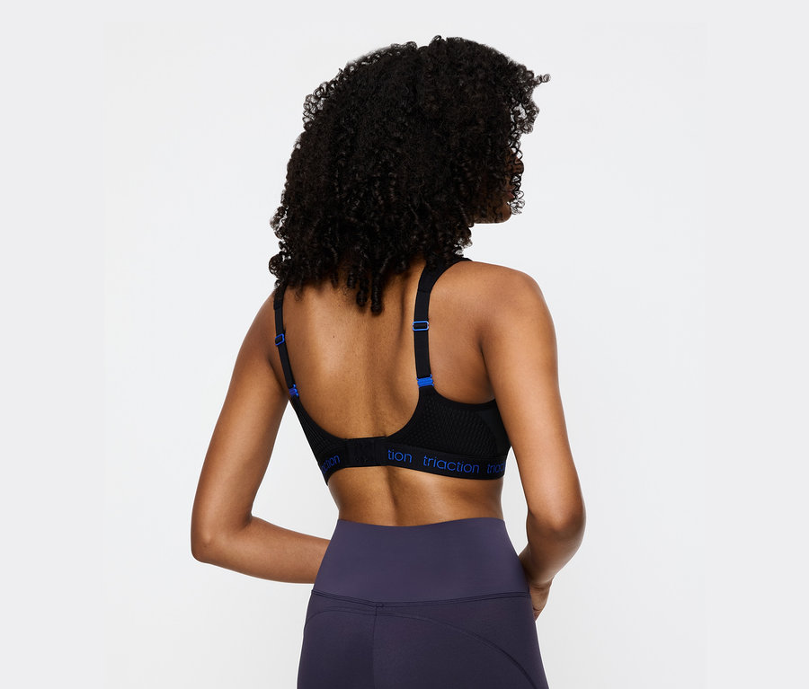 Rückansicht einer Frau mit lockigem Haar, die einen schwarzen Triaction Sport-BH und marineblaue Leggings trägt.