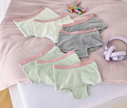 Auf einem Bett liegen sieben altrosa Mädchen-Pantys, ein Spielzeug und Kopfhörer.