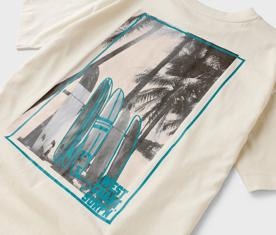 Auf einem cremefarbenen T-Shirt ist ein Rechteck mit Palmen und Surfbrettern aufgedruckt.