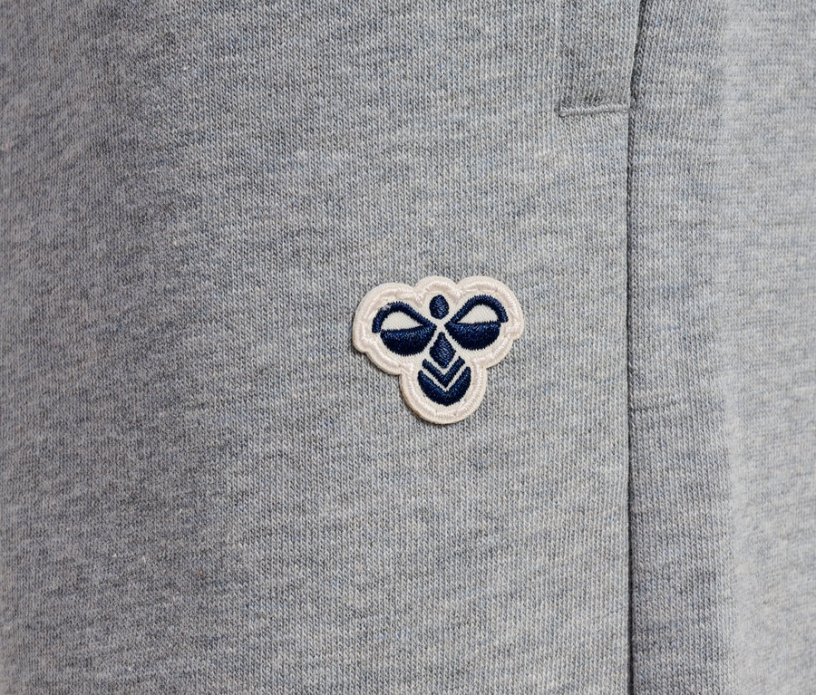 Detailaufnahme einer grauen Jogginghose mit einem kleinen, gestickten Logo.