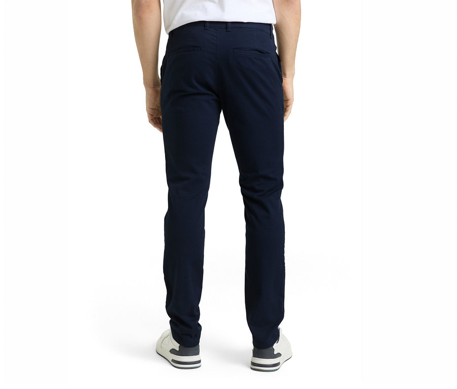 Eine Person von hinten, die eine dunkelblaue Hose und weiße Sneaker trägt, steht vor einem weißen Hintergrund.