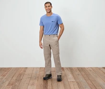 Ein Mann steht und trägt ein blaues T-Shirt, eine beige Hose und braune Schuhe.