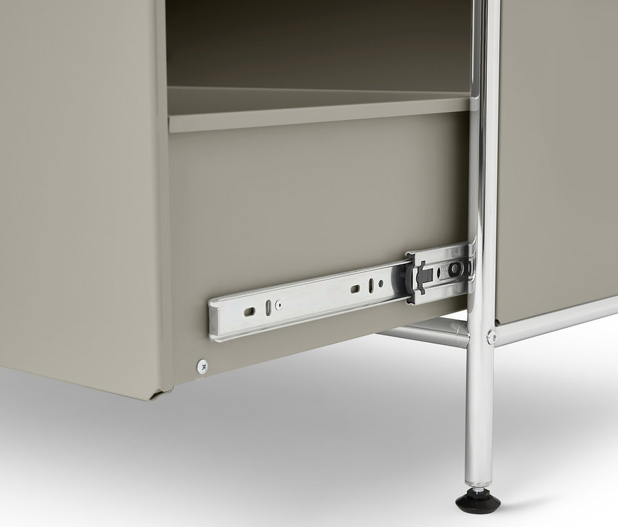 Nahaufnahme eines grauen Schranks mit teilweise ausgezogener Schublade, silbernen Metallschienen und einem verchromten Metallbein.