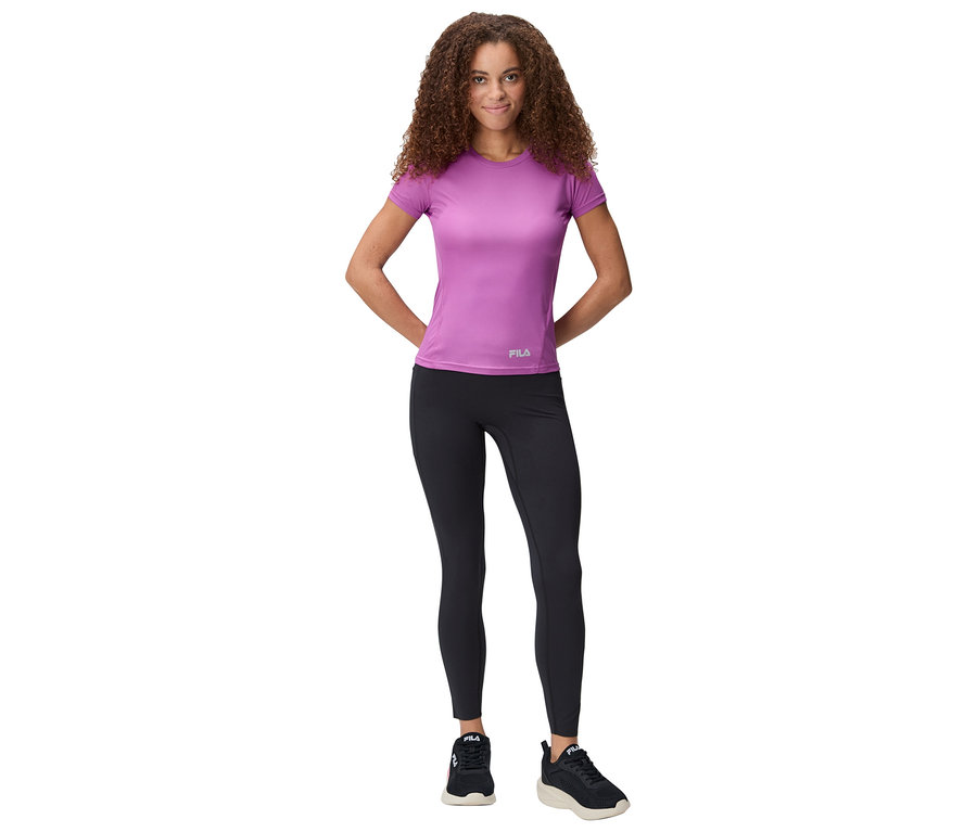 Frau steht mit den Händen hinter dem Rücken, trägt ein violettes T-Shirt, schwarze Leggings und Turnschuhe.