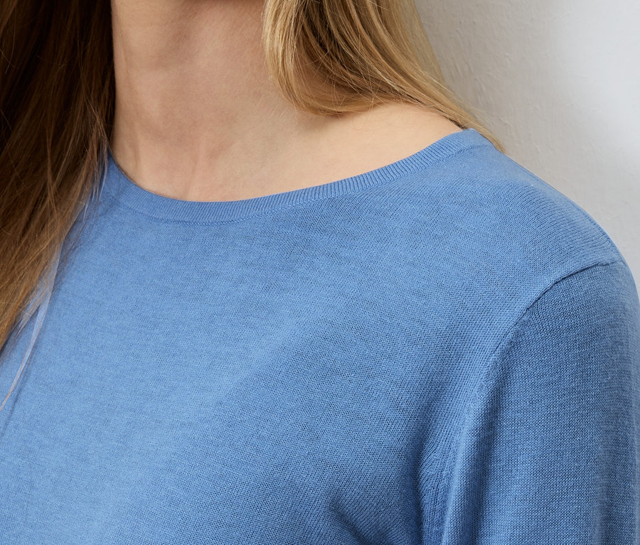 Nahaufnahme einer Frau mit blonden Haaren, die einen hellblauen Pullover trägt.