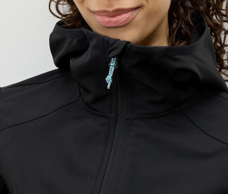 Nahaufnahme einer Frau mit lockigem Haar, die eine schwarze Kapuzenjacke mit blauem Reißverschluss trägt.