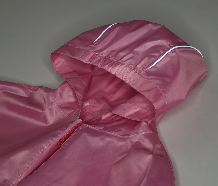 Nahaufnahme einer pinkfarbenen Jacke mit Kapuze und weißen Akzenten vor einem grauen Hintergrund.