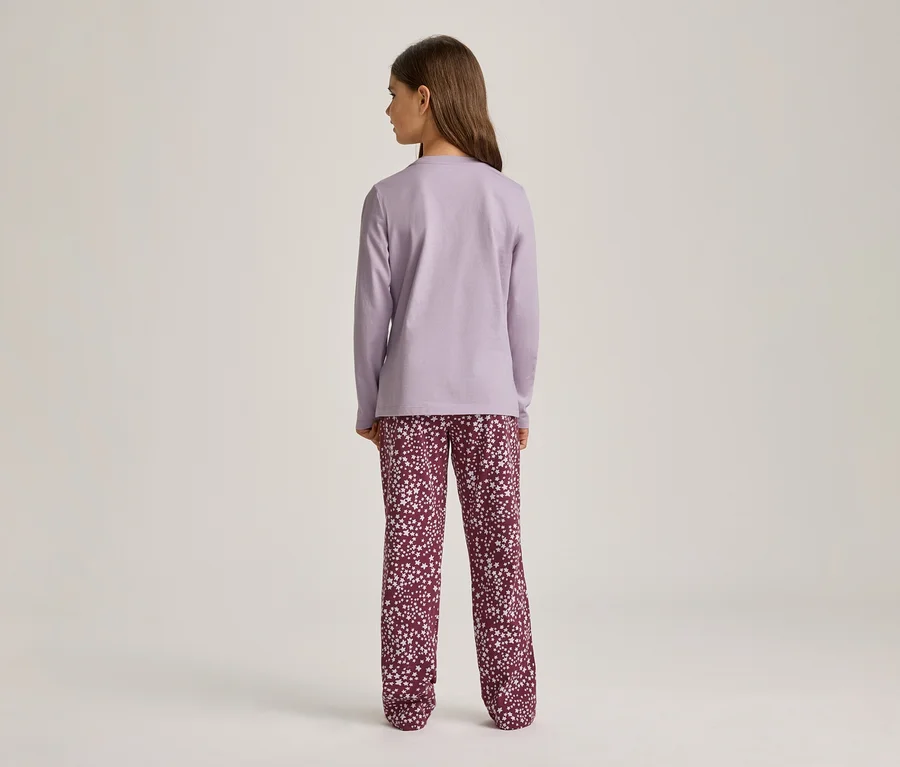 Eine Person steht mit dem Rücken zum Betrachter und trägt ein hellviolettes Langarmshirt und dunkelrote Hosen mit weißem Sternenmuster vor einem hellen Hintergrund.