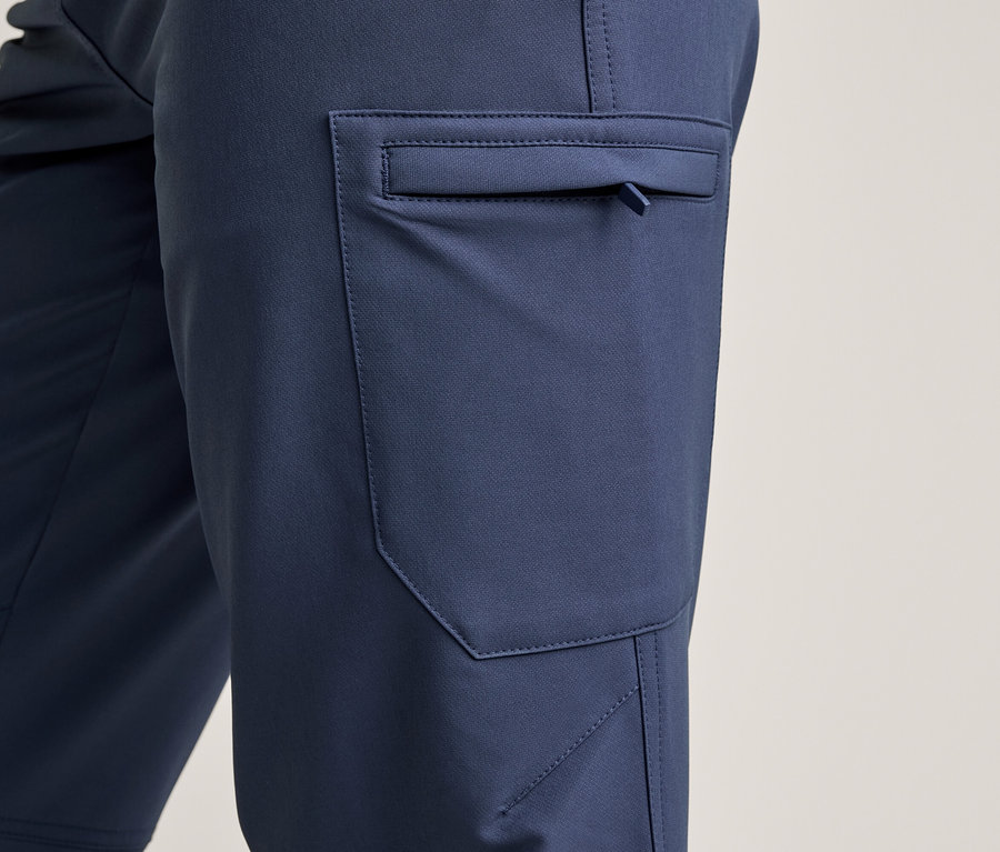 Nahaufnahme einer dunkelblauen Hose mit einer Cargotasche an der Seite, die einen kleinen Reißverschluss mit Zuglasche aufweist. Der Stoff ist glatt mit sichtbaren Nähten.