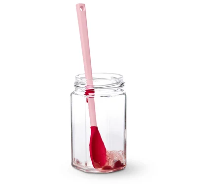 Ein rosa Teigschaber steht in einem leeren Glas.