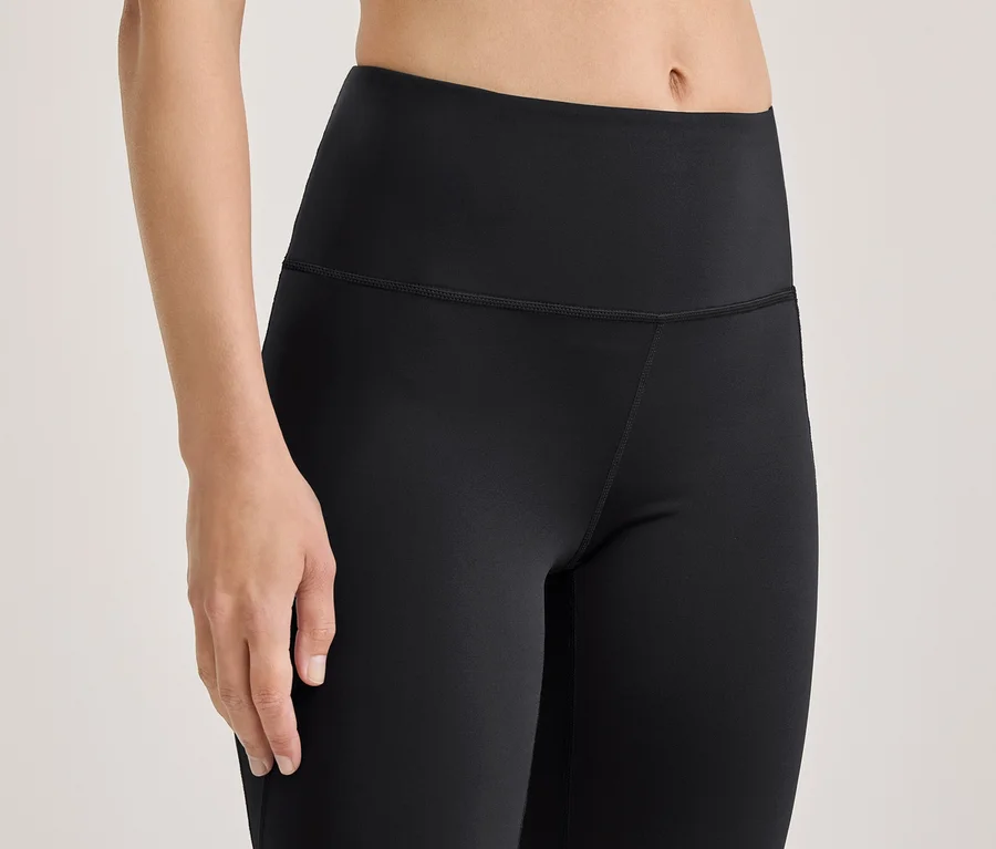 Nahaufnahme einer Person in schwarzen, hochgeschnittenen Leggings, die den Oberkörper, die Oberschenkel und den linken Arm zeigt.
