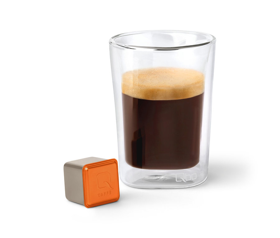Ein Glas Qbo Caffè MINAS VERDE neben einer Kapsel.