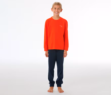 Lächelnder Junge in einem orangefarbenen SCHIESSER Kinder-Pyjama mit Bündchen und dunkelblauer Hose, barfuß stehend.