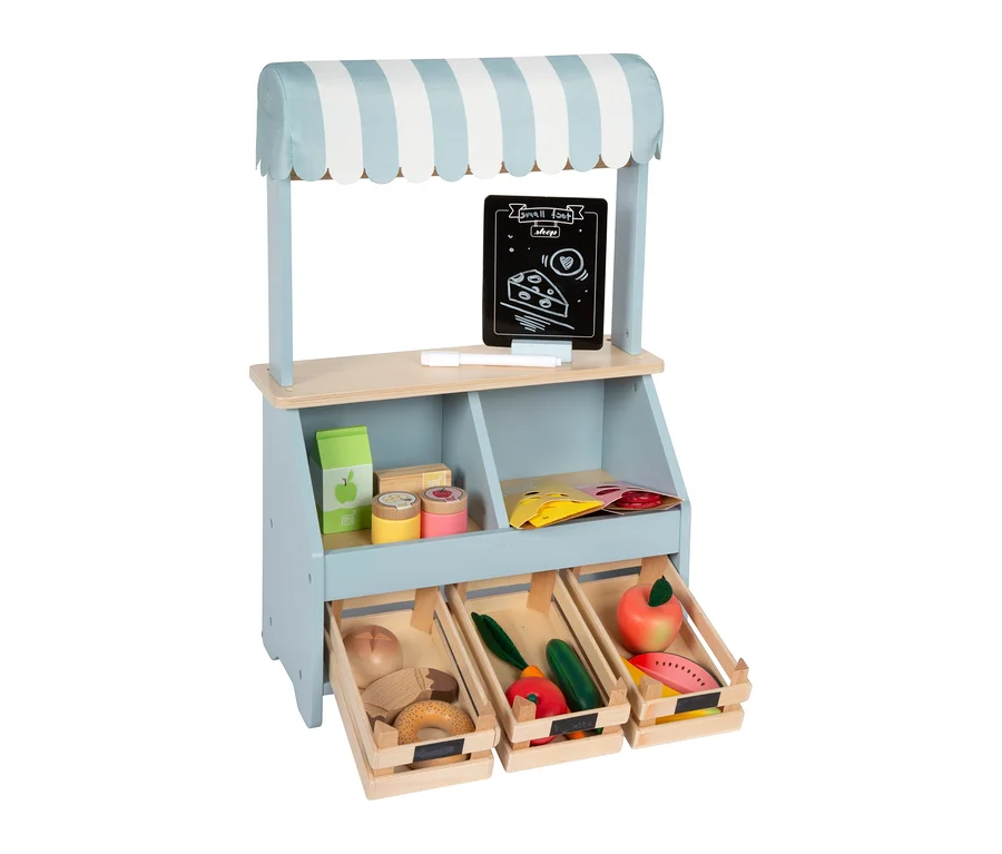 small foot kompakter Kaufladen, ein hellblauer Holz-Marktstand mit gestreifter Markise, der eine Tafel, Holz-Brot, Gemüse und Obst in Kisten zeigt.